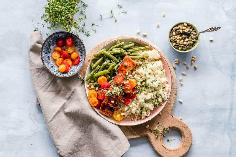 Helle Schüssel mit Couscous, grünen Bohnen und Tomaten auf einem hellen Tisch